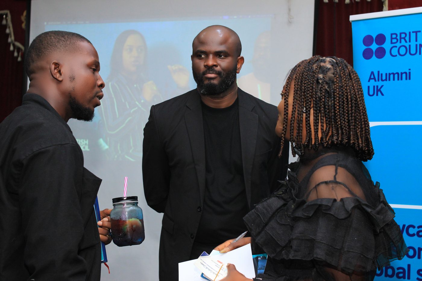 Three alumni in conversation beside the Alumni UK banner